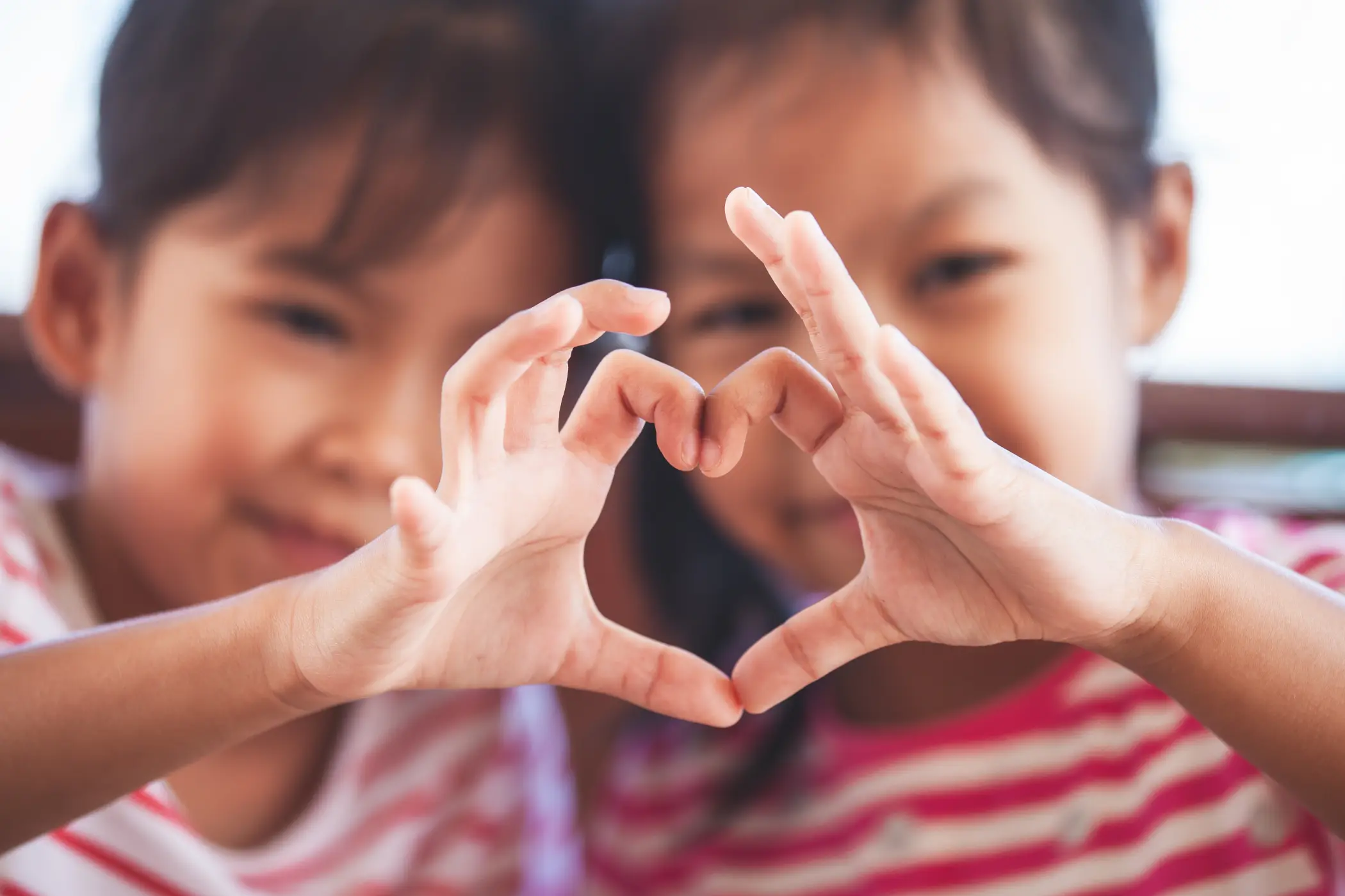 Two cute asian child girls making heart shape with hands