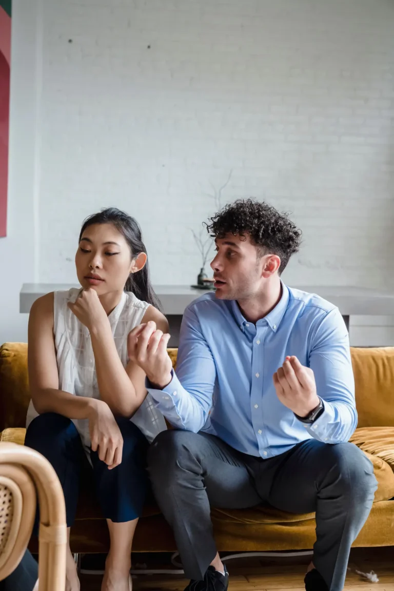 A couple sits indoors on a sofa, both appearing thoughtful and contemplative about divorce